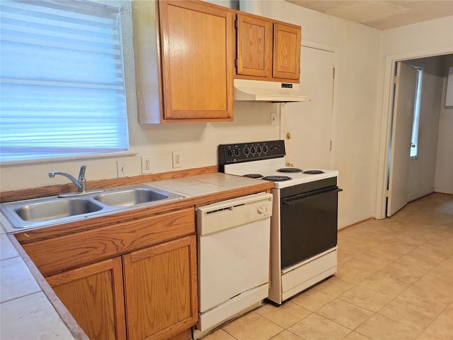 Kitchen with white appliances, under cabinet range hood, a sink, and tile countertops | Image 5