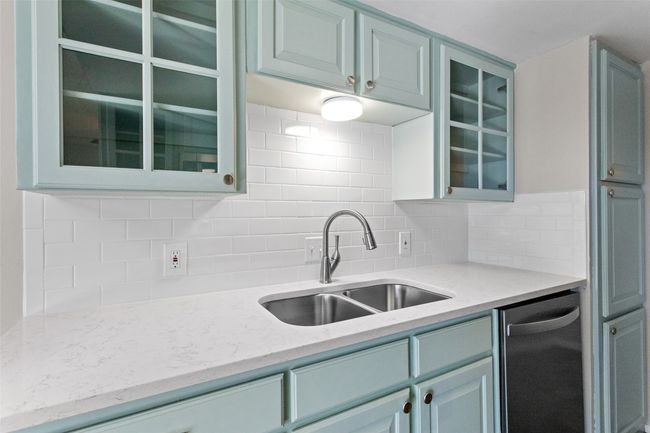 Kitchen with a sink, glass insert cabinets, light stone countertops, and backsplash | Image 13