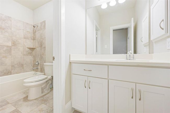 Clean and functional secondary bathroom with tile flooring, a large vanity, and a tub/shower combo with tiled surround. Neutral finishes offer a great foundation for future updates or personalization. | Image 33