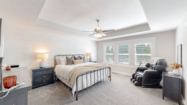 Carpeted bedroom featuring wood walls, a tray ceiling, baseboards, a textured ceiling, and a ceiling fan | Image 15