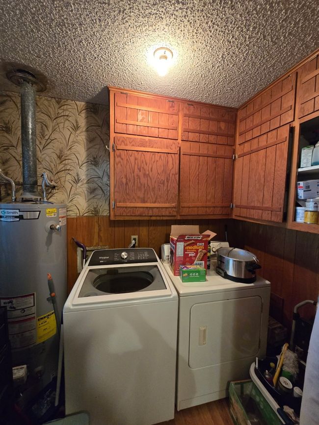 Laundry area featuring cabinet space, independent washer and dryer, gas water heater, wallpapered walls, and wooden walls | Image 28