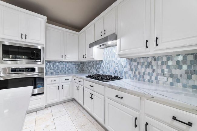 Kitchen with stainless steel oven, built in microwave, tasteful backsplash, under cabinet range hood, and black gas stovetop | Image 19