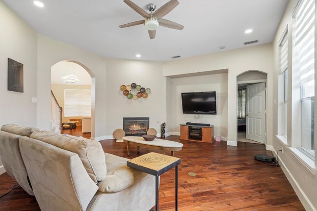 Living room with arched walkways, ceiling fan, wood finished floors, a glass covered fireplace, and recessed lighting | Image 13