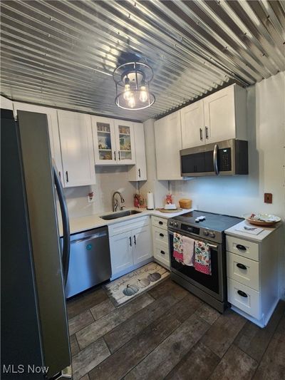 Kitchen featuring sink, dark wood-type flooring, white cabinetry and a notable chandelier | Image 3