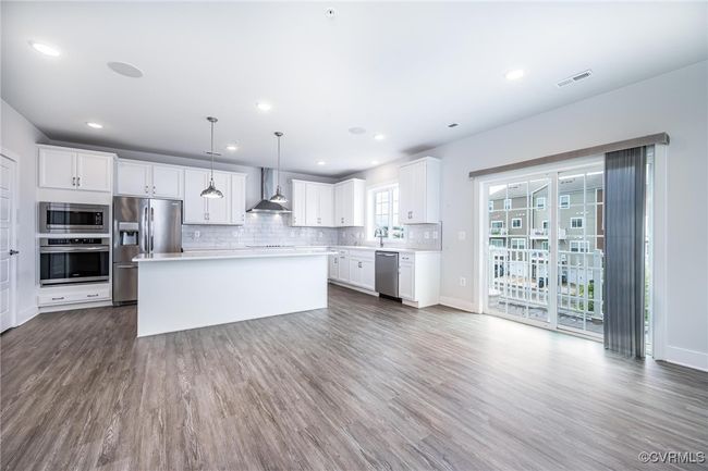 Kitchen featuring stainless steel appliances, wall chimney exhaust hood, dark wood-style flooring, white cabinets, and light countertops | Image 12