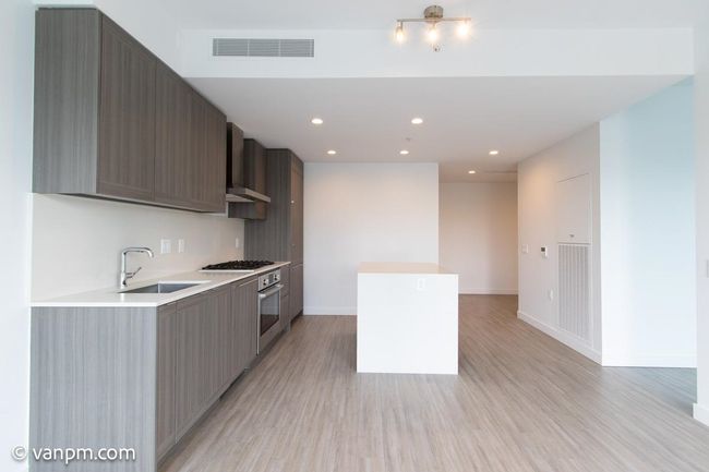 Kitchen with a sink, wall chimney range hood, stainless steel oven, light wood-style floors, and recessed lighting | Image 15