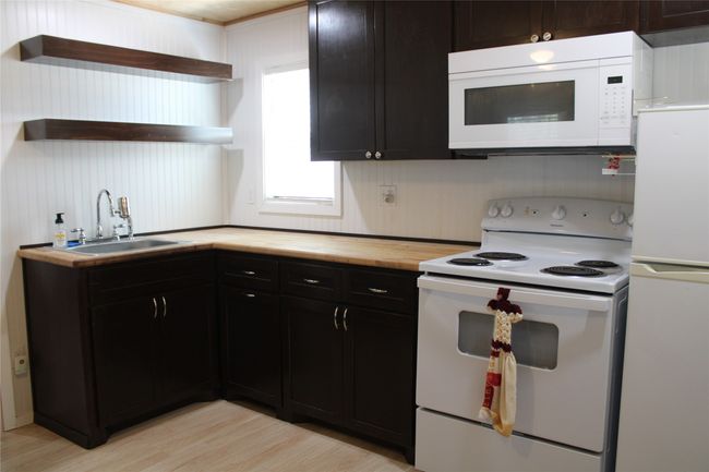 Kitchen with white appliances, open shelves, a sink, wood counters, and light wood-type flooring | Image 5