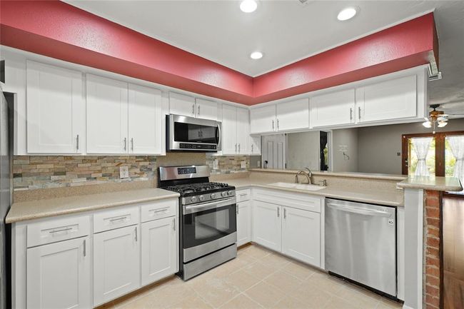 This modern kitchen features sleek white cabinetry, stainless steel appliances, and a stone tile backsplash. | Image 14