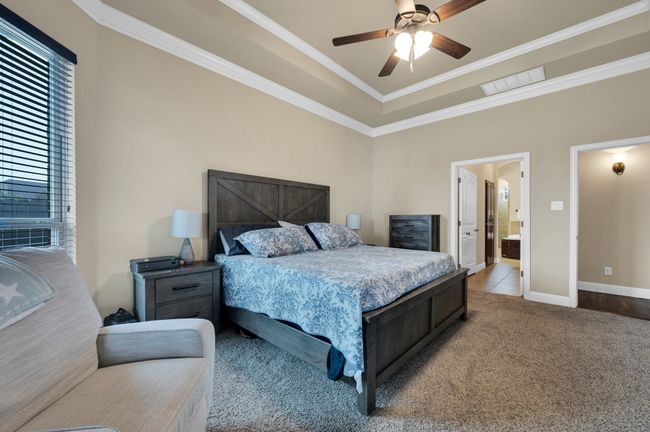 Carpeted bedroom featuring a tray ceiling, baseboards, crown molding, ceiling fan, and ensuite bathroom | Image 17