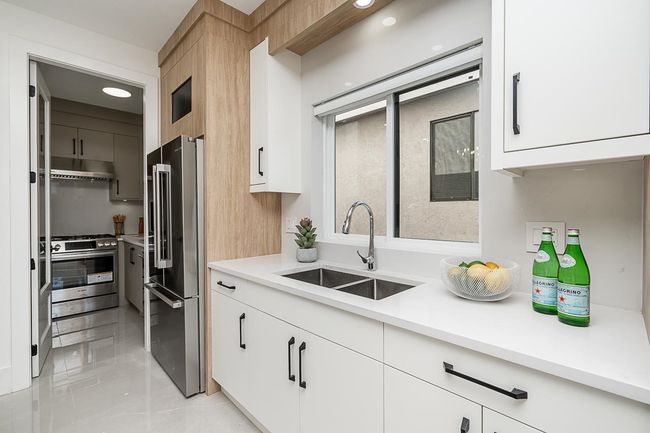 Kitchen featuring high end refrigerator, a sink, stainless steel gas range oven, under cabinet range hood, and light countertops | Image 6