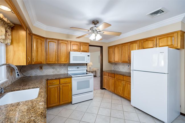 Kitchen with dark stone countertops, white appliances, a sink, visible vents, and a ceiling fan | Image 17
