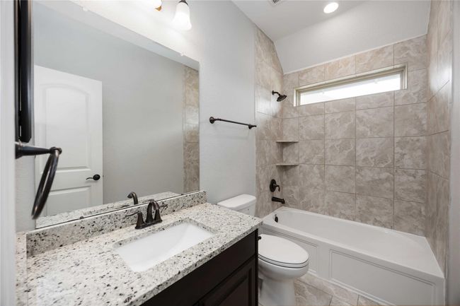 This bathroom features a sleek design with a granite countertop, dark wood vanity, and modern fixtures. It includes a tiled bathtub/shower combo and a large mirror, offering a clean and elegant look. | Image 28