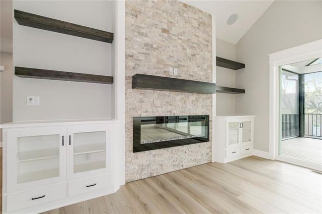 Unfurnished living room featuring vaulted ceiling, wood finished floors, a stone fireplace, and baseboards | Image 5
