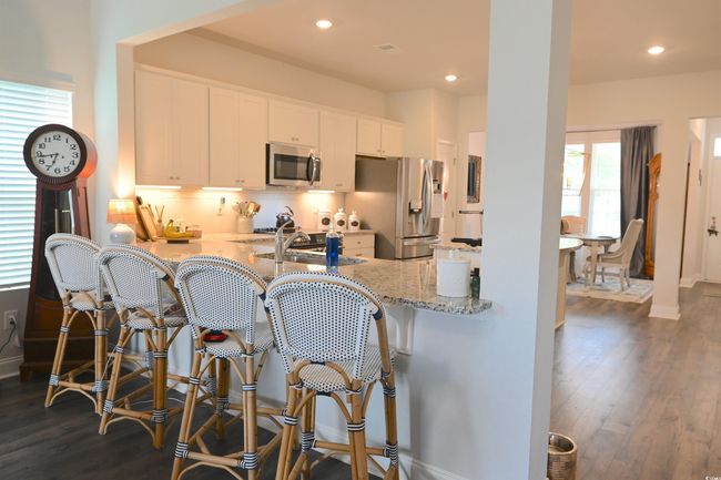 Kitchen with a peninsula, stainless steel appliances, dark wood finished floors, light stone counters, and white cabinets | Image 10