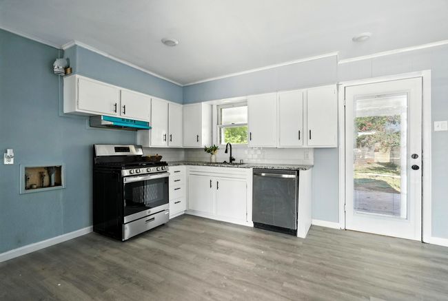 Kitchen with stainless steel appliances, under cabinet range hood, light wood-style flooring, white cabinets, and ornamental molding | Image 7