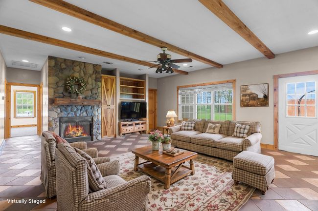 Living room featuring baseboards, a stone fireplace, beamed ceiling, and ceiling fan | Image 19