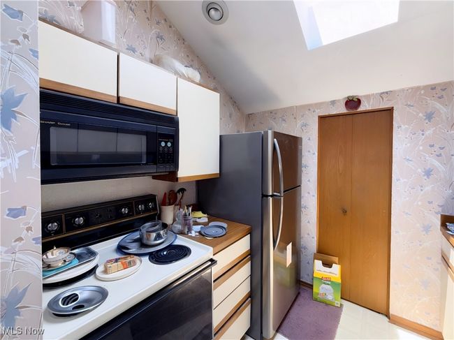 Kitchen with electric stove, black microwave, wallpapered walls, a skylight, and lofted ceiling | Image 18