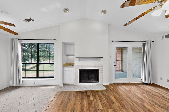 Unfurnished living room featuring a ceiling fan, vaulted ceiling, a tiled fireplace, baseboards, and wood finished floors | Image 13