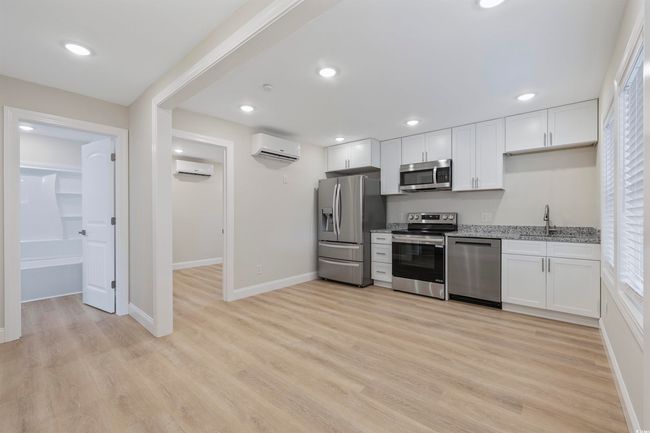 Kitchen featuring appliances with stainless steel finishes, a wall unit AC, light stone counters, white cabinets, and recessed lighting | Image 23