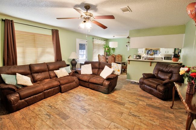 Living area with a textured ceiling, visible vents, a ceiling fan, and wood finished floors | Image 6