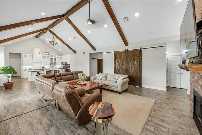Living area featuring a barn door, a fireplace, beamed ceiling, light wood-type flooring, and high vaulted ceiling | Image 4