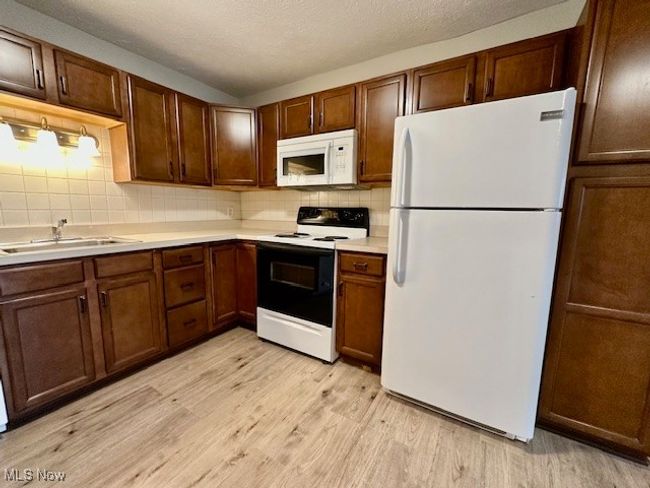 Kitchen with white appliances, light wood-style flooring, a sink, decorative backsplash, and light countertops | Image 10