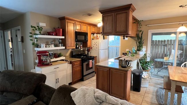 Kitchen with gas stove, black microwave, freestanding refrigerator, light tile patterned flooring, and a peninsula | Image 14