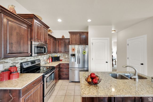 Kitchen with appliances with stainless steel finishes, light tile patterned floors, tasteful backsplash, light stone counters, and dark brown cabinetry | Image 6