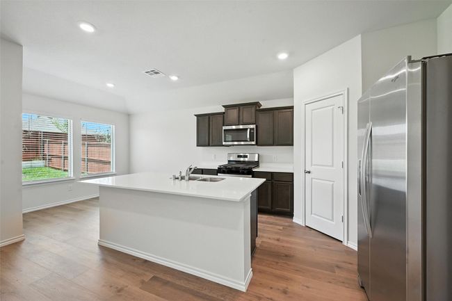Kitchen featuring stainless steel appliances, wood finished floors, light countertops, an island with sink, and recessed lighting | Image 8