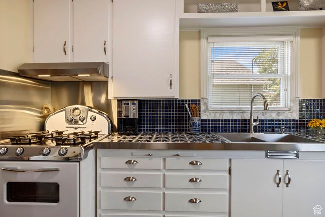 Kitchen featuring stainless steel gas range oven, wall chimney exhaust hood, white cabinetry, and backsplash | Image 4
