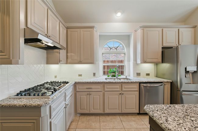 Kitchen featuring under cabinet range hood, appliances with stainless steel finishes, light tile patterned floors, and light stone counters | Image 10