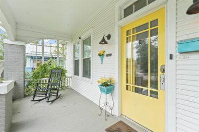 Cozy covered front porch featuring a rocking chair, bright yellow door with glass panels, and charming decorative accents, providing a welcoming entrance to the home. | Image 2