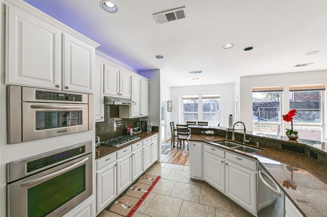 Kitchen featuring white cabinetry, appliances with stainless steel finishes, sink, tasteful backsplash, and light tile floors | Image 10