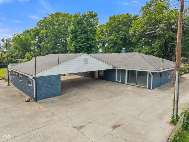 ranch-style home featuring concrete driveway, a carport, roof with shingles, a chimney, and view of scattered trees | Image 51