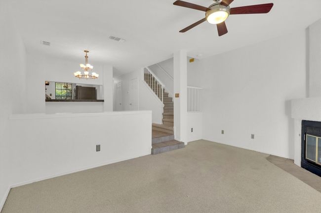 Unfurnished living room with stairs, ceiling fan with notable chandelier, a fireplace with flush hearth, carpet, and visible vents | Image 14