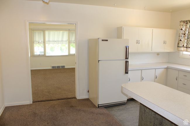 Kitchen with freestanding refrigerator, light countertops, white cabinetry, and dark carpet | Image 28