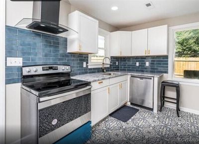 Kitchen featuring stainless steel appliances, white cabinets, light tile patterned floors, sink, and wall chimney range hood | Image 3