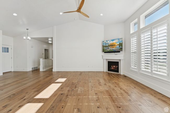 Unfurnished living room featuring a lit fireplace, light wood-type flooring, a ceiling fan, a chandelier, and recessed lighting | Image 5
