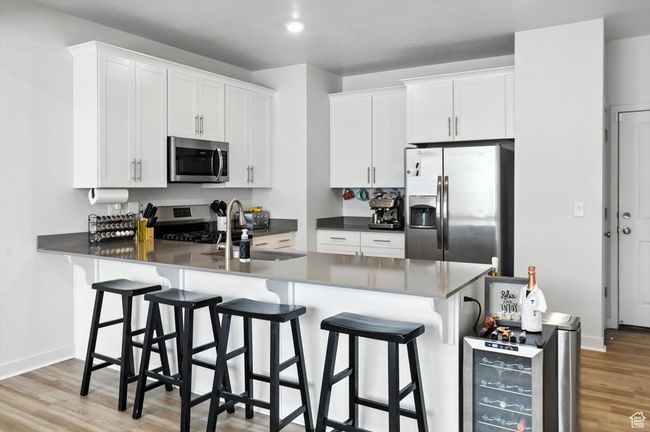 Kitchen featuring stainless steel appliances, new light wood-style LVP floors, white cabinetry, a kitchen bar, and a peninsula | Image 28