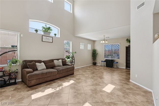 Living area with a towering ceiling, a chandelier, light tile patterned floors, and baseboards | Image 9