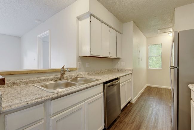 Kitchen with appliances with stainless steel finishes, a sink, a textured ceiling, wood finished floors, and light countertops | Image 8