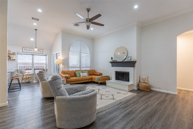 Living area featuring a ceiling fan, dark wood-style flooring, arched walkways, a brick fireplace, and crown molding | Image 8