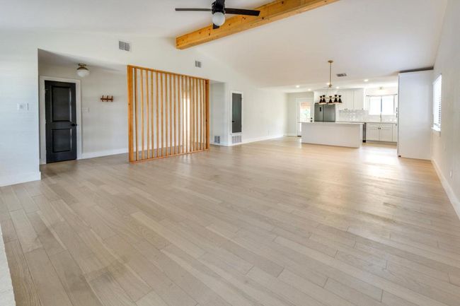 Unfurnished living room featuring visible vents, lofted ceiling with beams, a ceiling fan, and light wood finished floors | Image 9