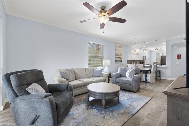 Living room featuring ceiling fan with notable chandelier, ornamental molding, and light lvp wood-type flooring | Image 10