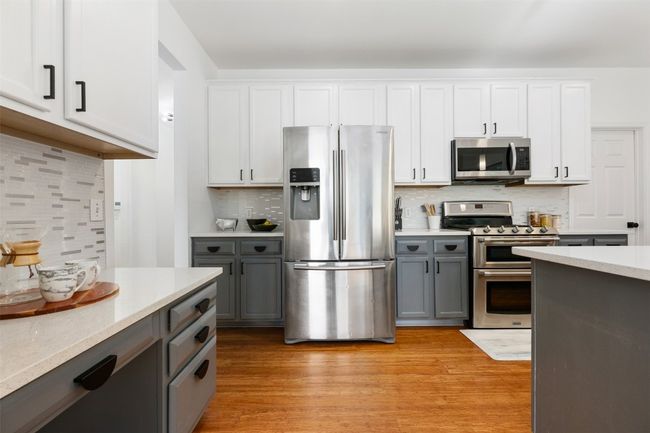 Kitchen featuring light wood-type flooring, gray cabinets, backsplash, white cabinets, and stainless steel appliances | Image 10