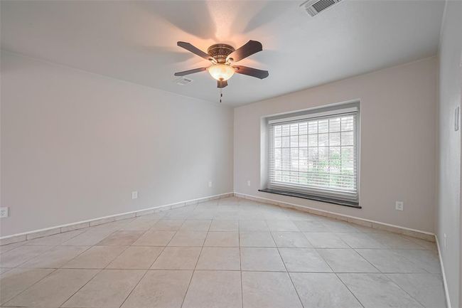 A cozy sitting area just off the entryway features a large front-facing window with deep ledge seating, perfect for relaxing with a view. Neutral tile floors and a ceiling fan make this space versatile for a study, reading nook, or playroom. | Image 8