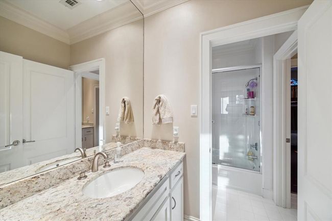 This bathroom features a granite countertop with dual sinks, a large mirror, and a glass-enclosed shower. The neutral color palette and ample lighting create a clean and inviting atmosphere. | Image 26
