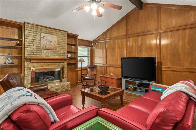 Living room featuring wood finished floors, a ceiling fan, wooden walls, a brick fireplace, and built in features | Image 10