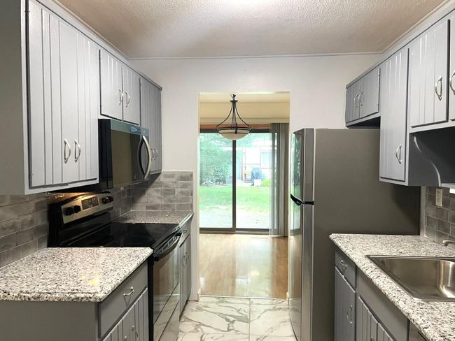 Kitchen with appliances with stainless steel finishes, gray cabinets, light marble finish flooring, backsplash, and a textured ceiling | Image 6