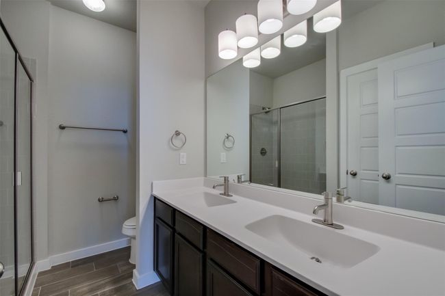 Full bathroom with a shower stall, double vanity, toilet, wood finish floors, and baseboards | Image 13